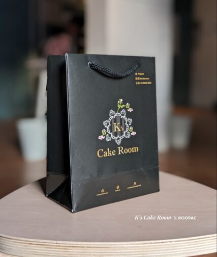 A close-up of a sturdy paper bag featuring the K's Cake Room logo, ideal for safely transporting and storing cakes