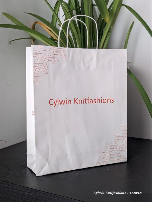 A Cylwin Knitfashions Special Paper Bag showcasing the bright red logo against a white background