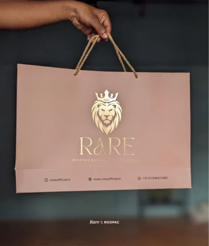 RARE's luxury gold-foiled paper bag with a lion face logo on pastel pink, Coimbatore